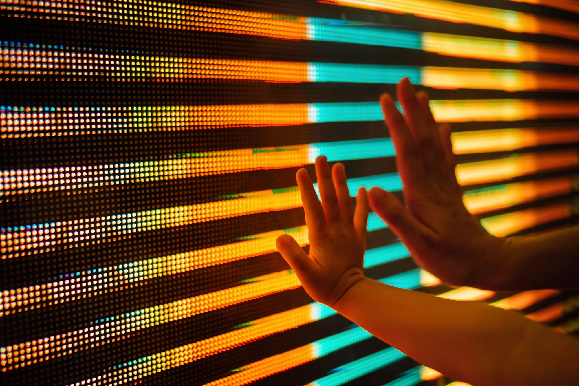 Close up of a mother and kid's hand touching illuminated and multi-coloured LED display screen, connecting to the future